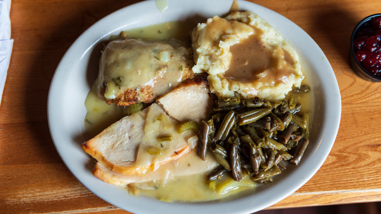 Turkey, mashed potatoes, green beans, and gravy on a white plate placed on a wooden table