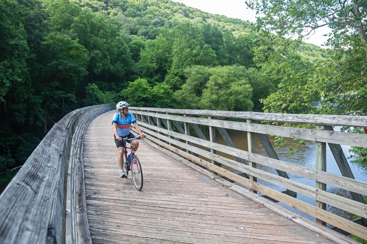 Christian Jones cycling on a wooden bridge surrounded by trees in a park setting