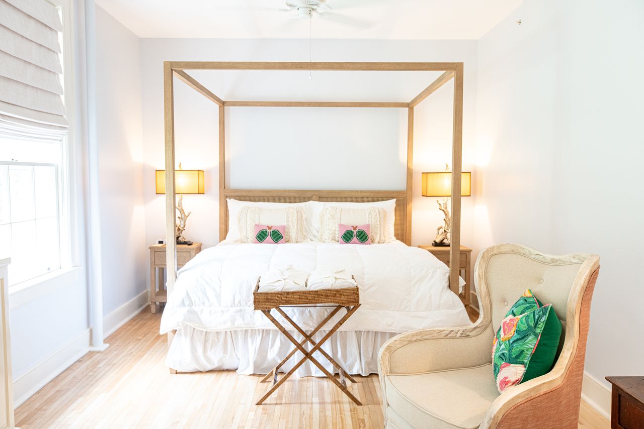 A bedroom with a canopy bed accent armchair and wooden nightstands designed in a minimalist style