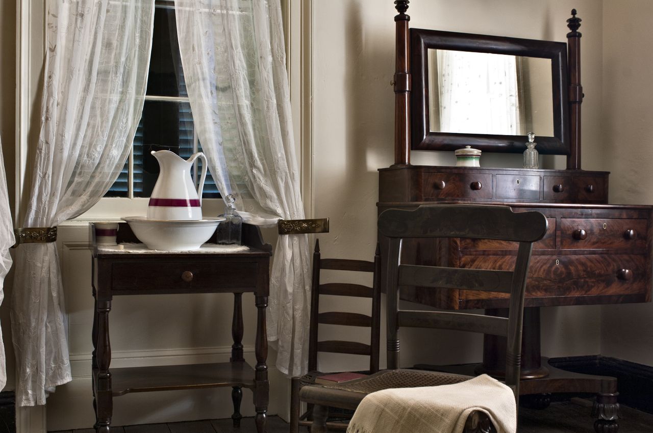 A vintagestyle bedroom scene with wooden furniture including a dresser with a mirror and a table holding a ceramic pitcher