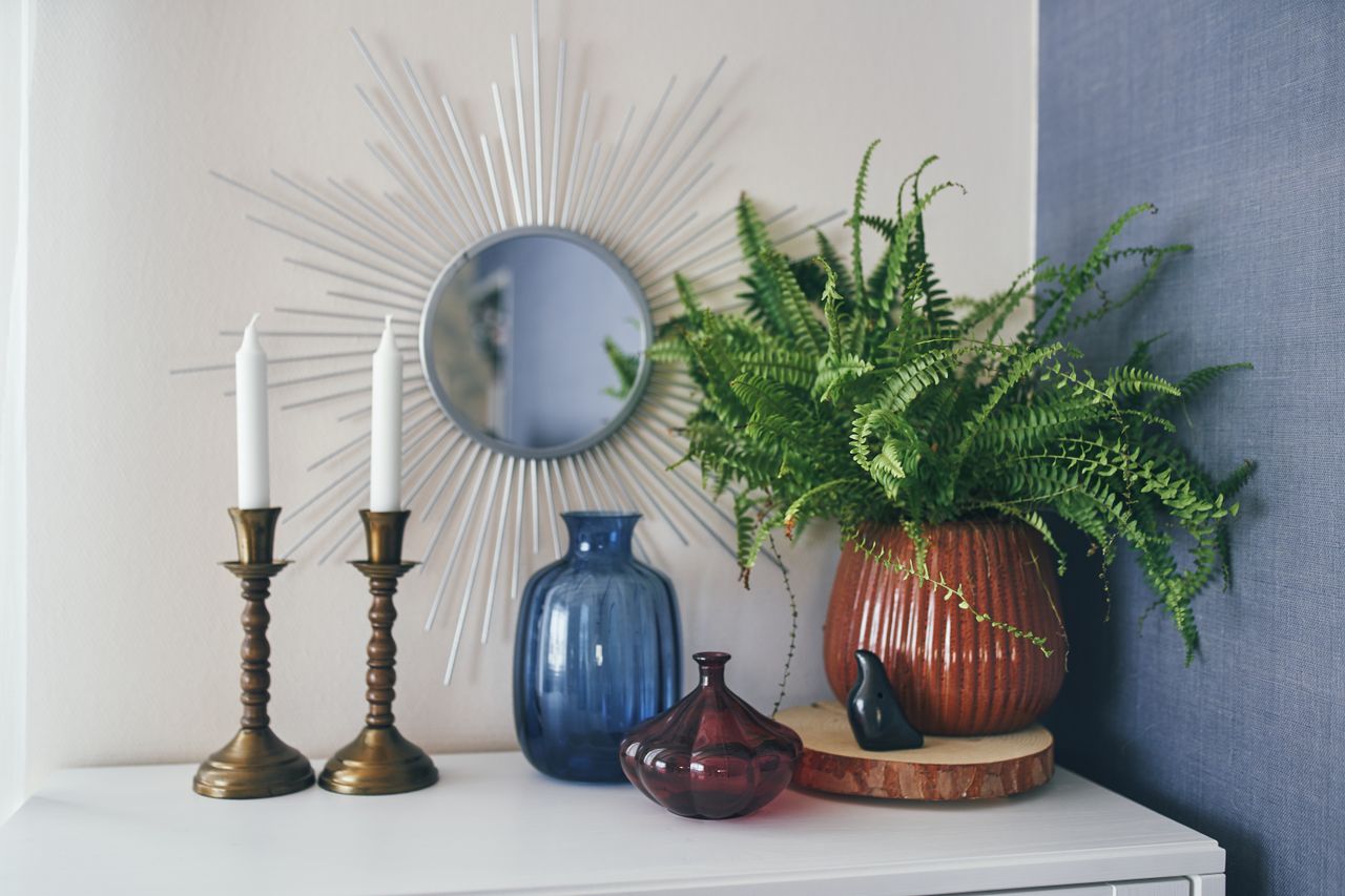 A decorative arrangement on a table including a starshaped mirror two candlesticks vases and a potted plant