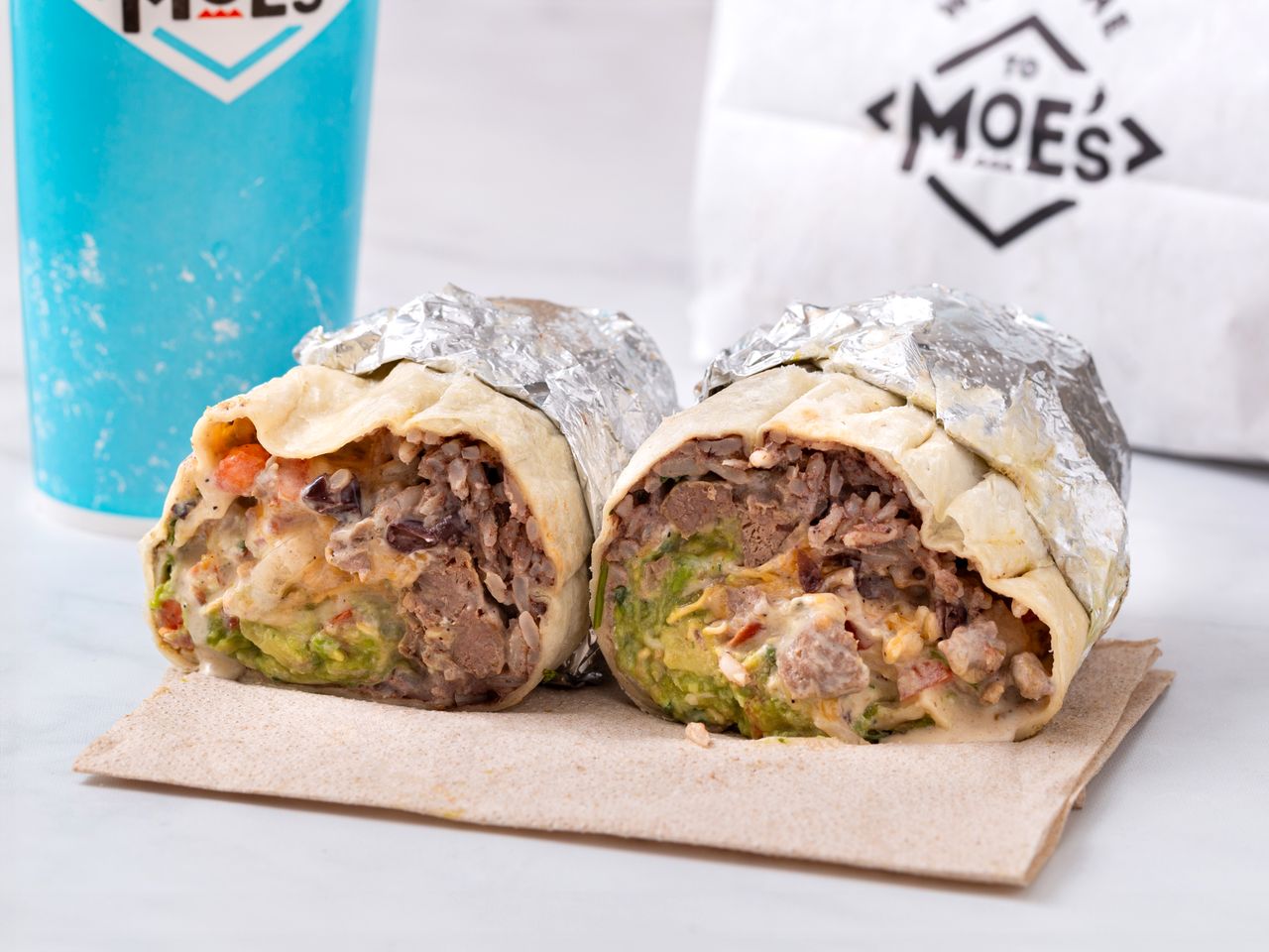 A sirloin steak burrito from Moe's! Southwest Grill, cut in half, with a drink in the background