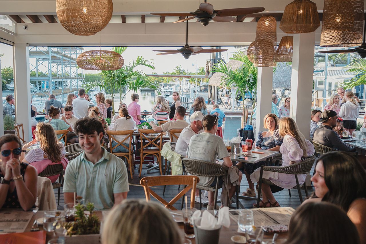 People dining at an outdoor waterfront restaurant lively setting with tables chairs and greenery