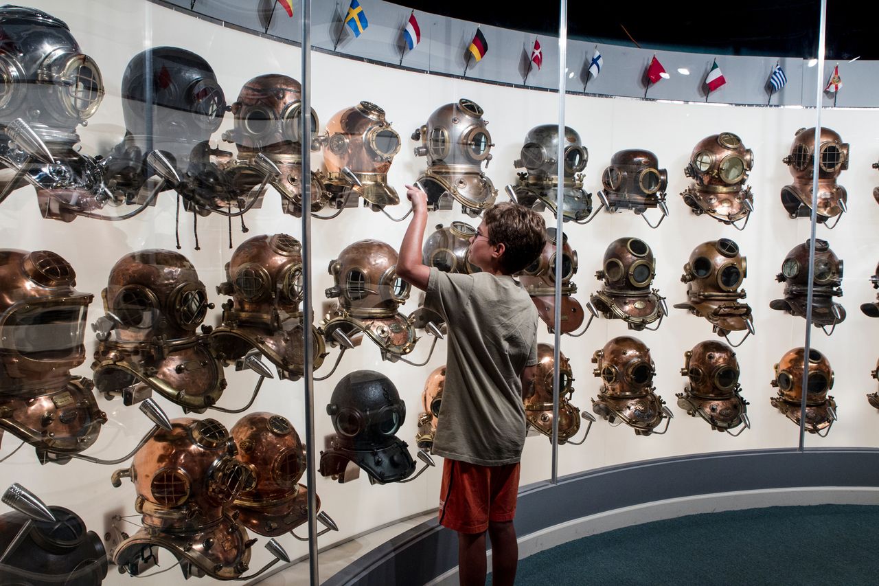 A person examining a display of vintage diving helmets in a museum exhibit