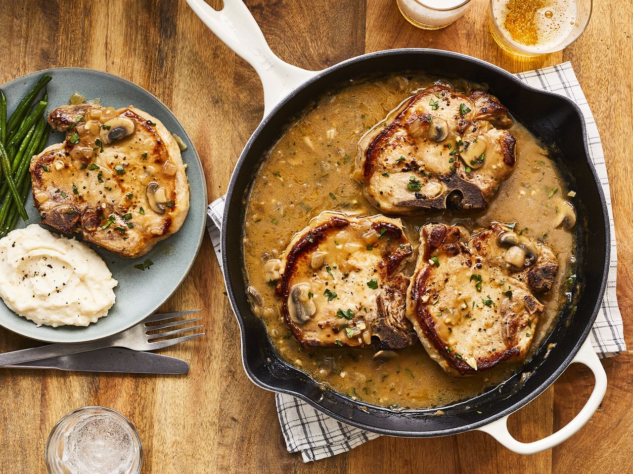 close up view of Southern Smothered Pork Chops in Brown Gravy in a pan, and a pork chop with mashed potatoes and green beans on a plate
