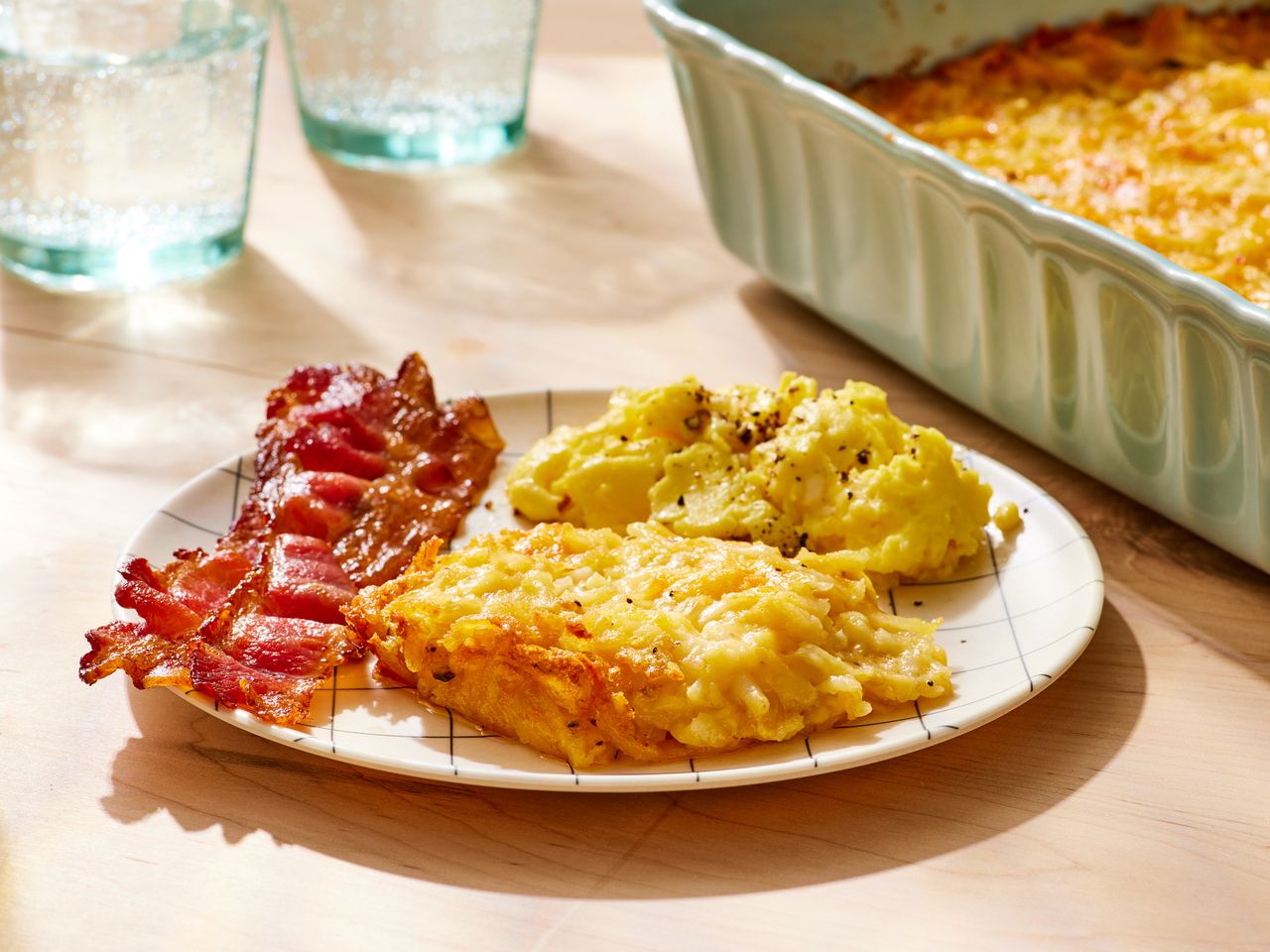 A plate with restaurant-style hash brown casserole, crispy, and scrambled eggs, with a baking dish of hash brown casserole in the background