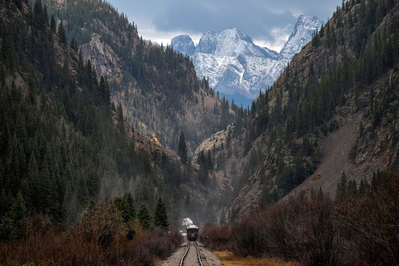Train traveling through a mountain valley with snowy peaks in the background