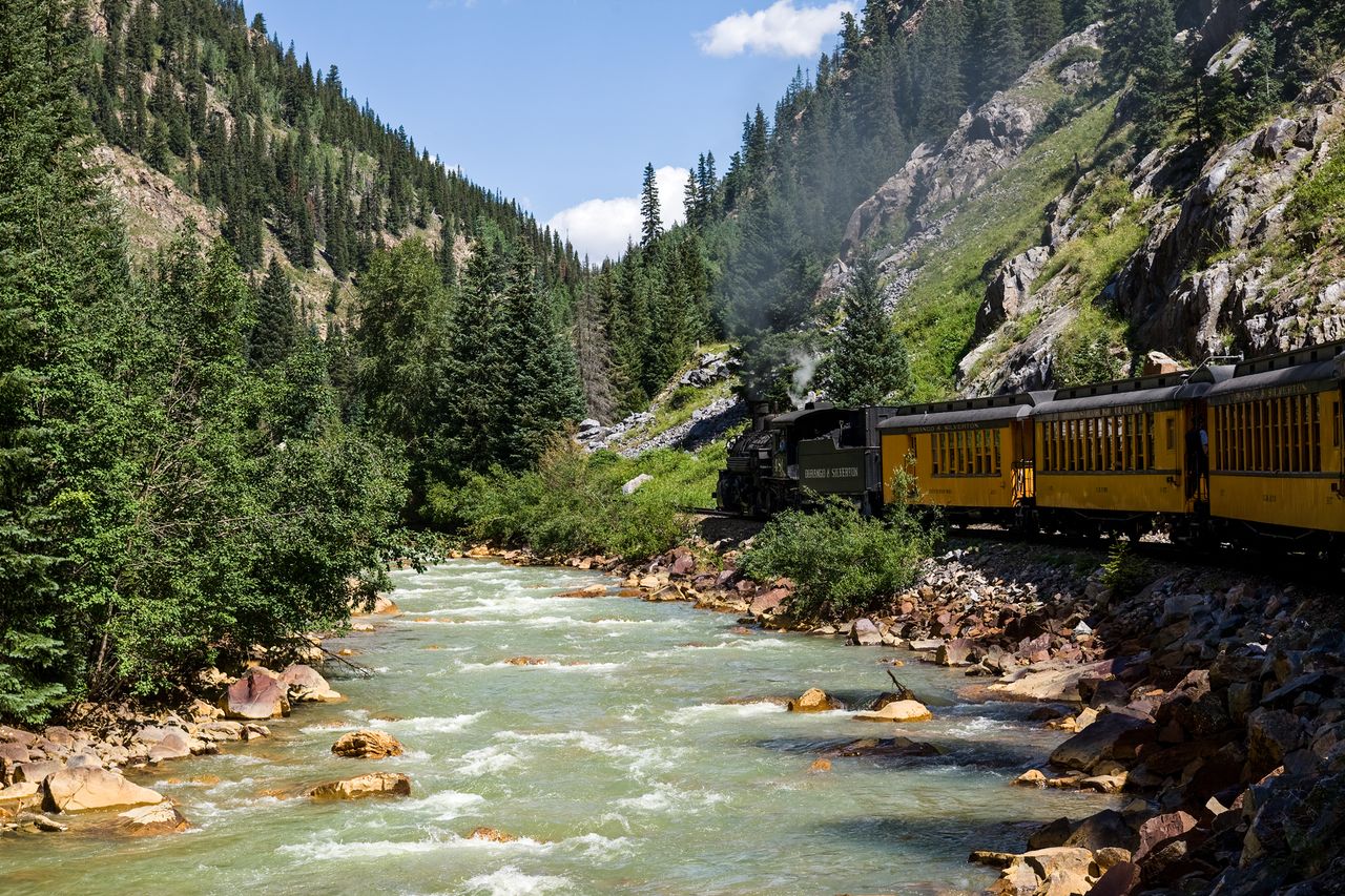 A steam train running along a river in a mountain valley