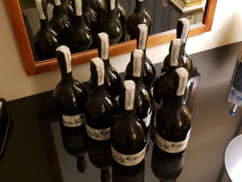 Nine bottles of sparkling wine on a reflective surface, organized in rows with visible labels