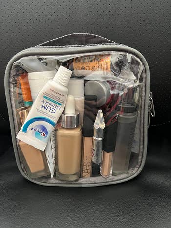 Clear toiletry bag filled with various travel-sized skincare and makeup products, including lotions, foundation, and a tube of gum protection product