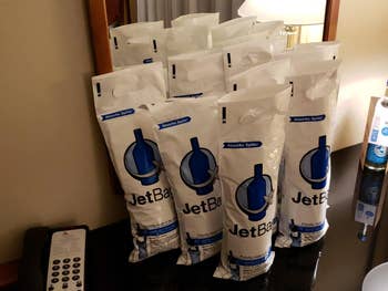 Several JetBag absorbent travel bags displayed on a table near a hotel room mirror, designed to protect and contain bottles during travel
