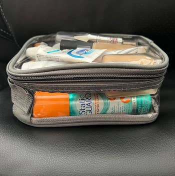 Clear travel toiletry bag filled with a variety of travel-sized personal care items, including toothpaste, foundation, and skincare products
