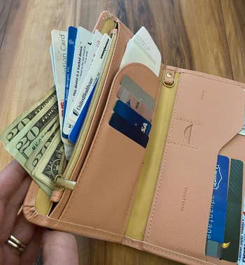An open wallet with various credit cards, cash, and receipts displayed, held by a person with a ring on their finger