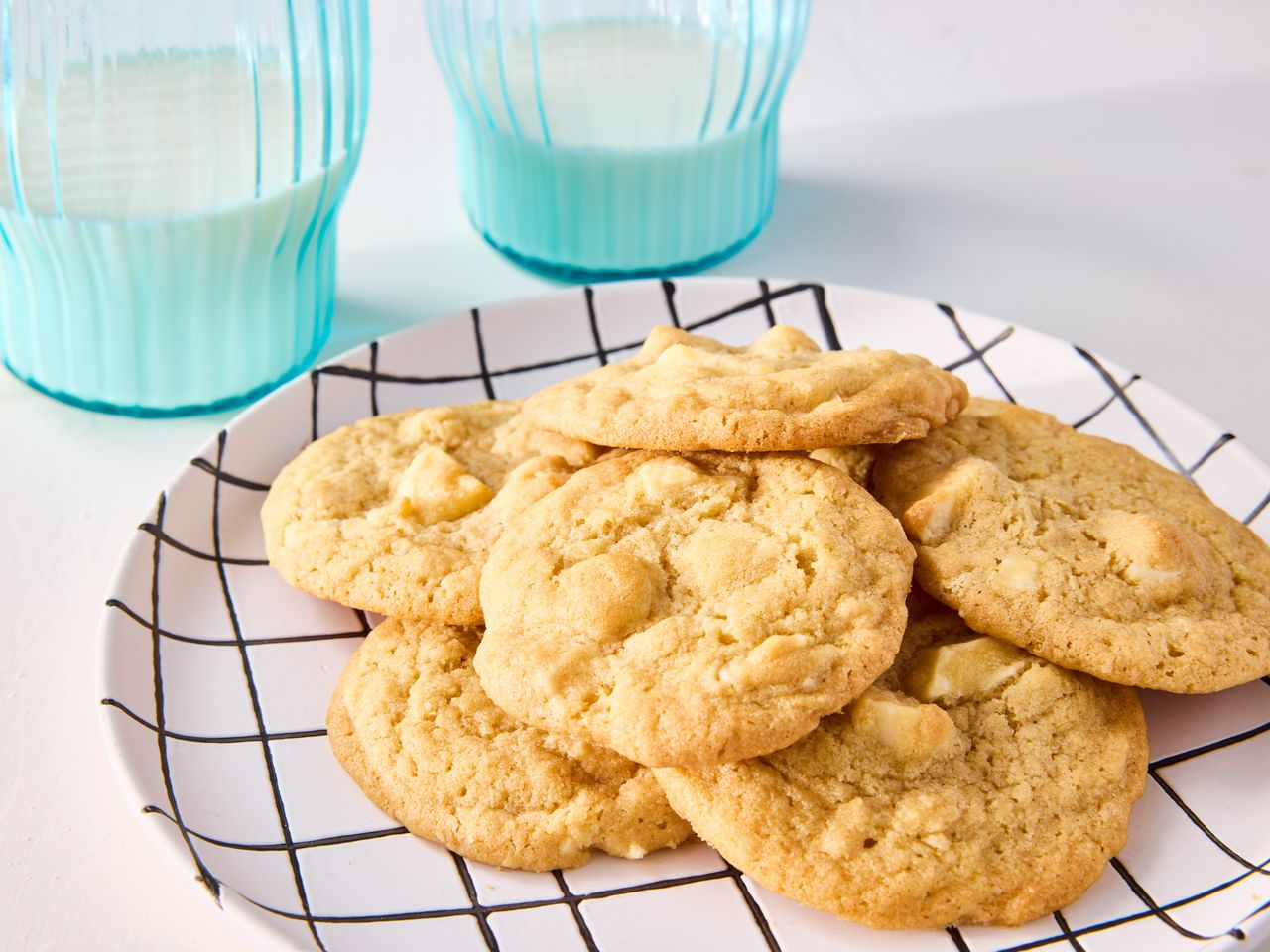 A plate with white chocolate macadamia nut cookies, served with two glasses of milk