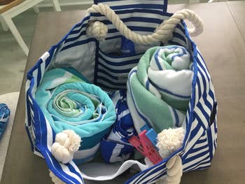 A striped beach bag holds rolled towels and clothespins, placed on a wooden surface