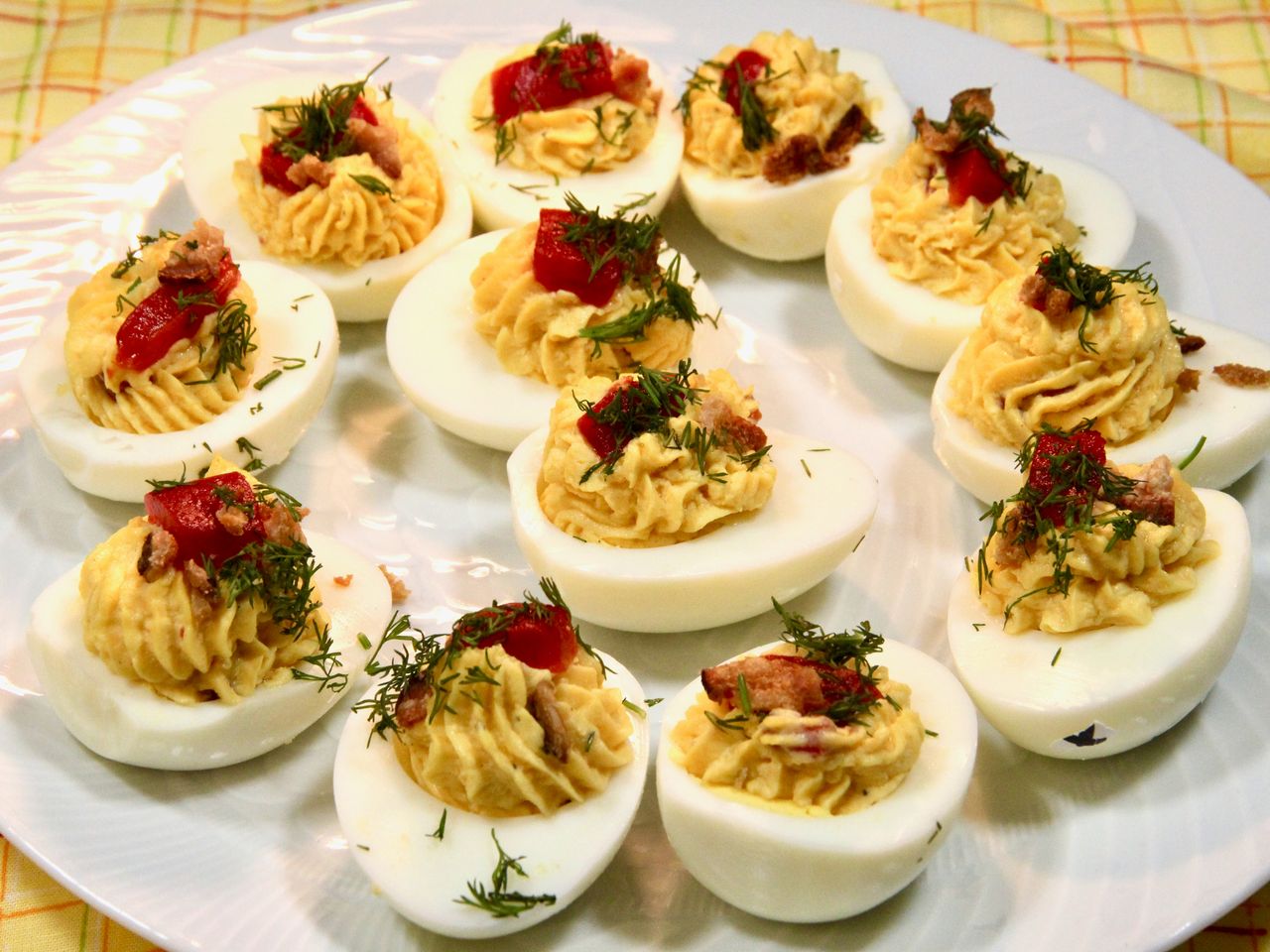 deviled eggs arranged on a white plate with pimento and dill sprinkled over