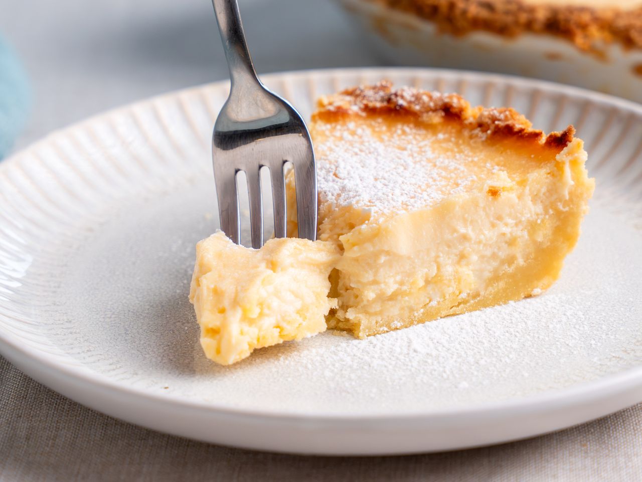 A slice of ricotta pie on a white plate with a fork taking a bite