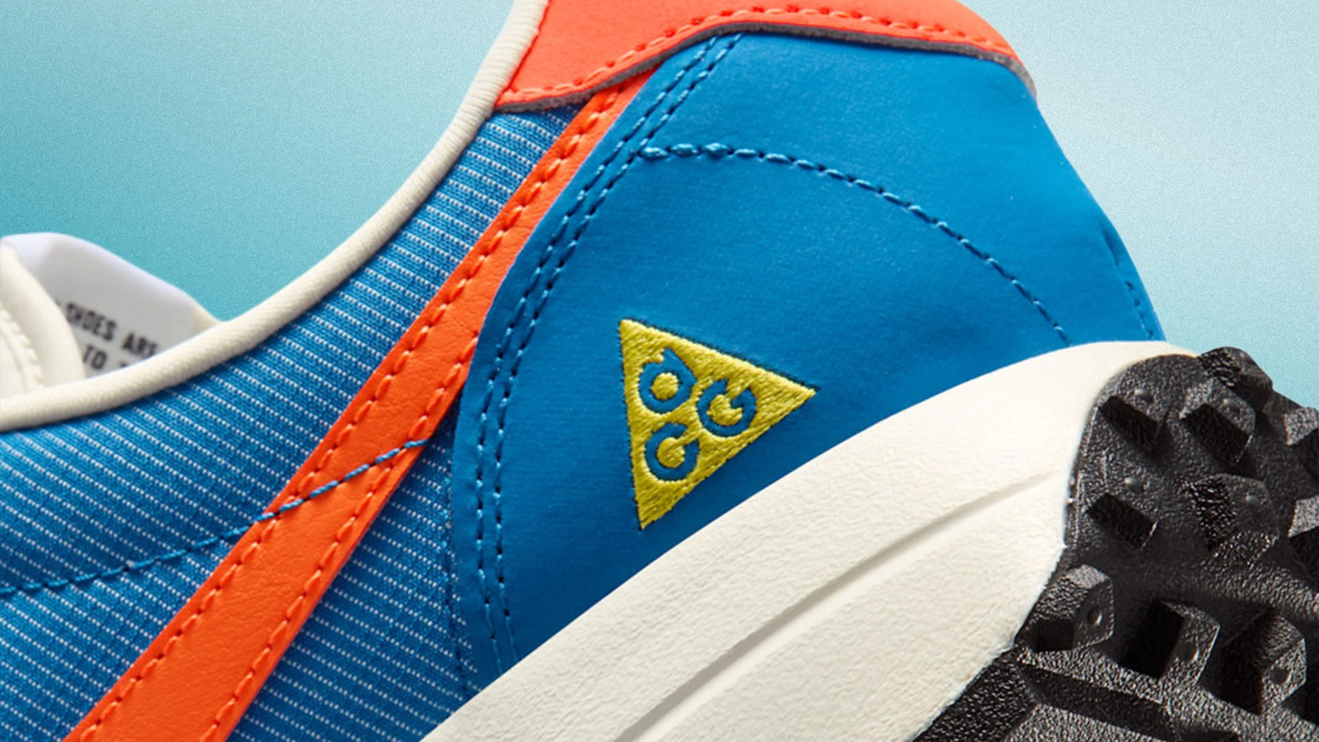 Close-up of a blue and orange sneaker heel with a yellow triangular logo and a white midsole with black textured outsole.