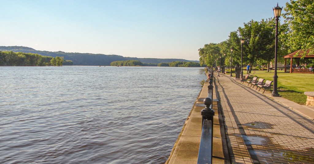 Paved riverfront path with benches on St. Feriole Island in Prairie du Chien, WI, at sunset.