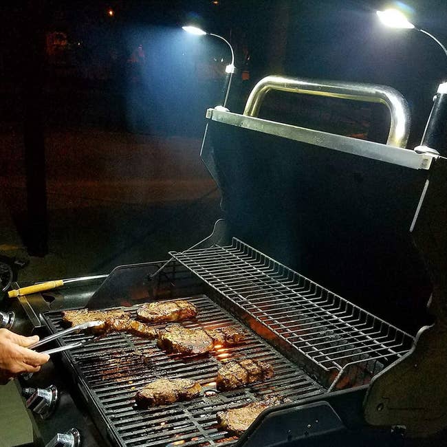 Model grilling meat on a barbecue at night while using the lights, magnetically attached to the grill
