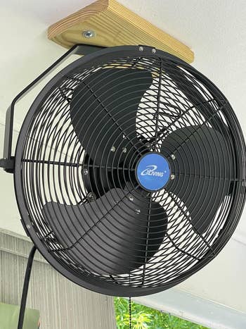 Wall-mounted industrial fan in a room setting, showcasing its sturdy design. Ideal for enhancing air circulation in larger spaces