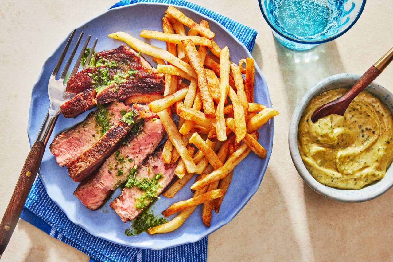 Steak Frites on a blue plate with mustard sauce in a bowl