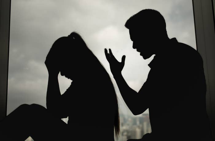 Silhouettes of a person sitting with their head in hands, appearing distressed, while another stands, gesturing emphatically in front of a window