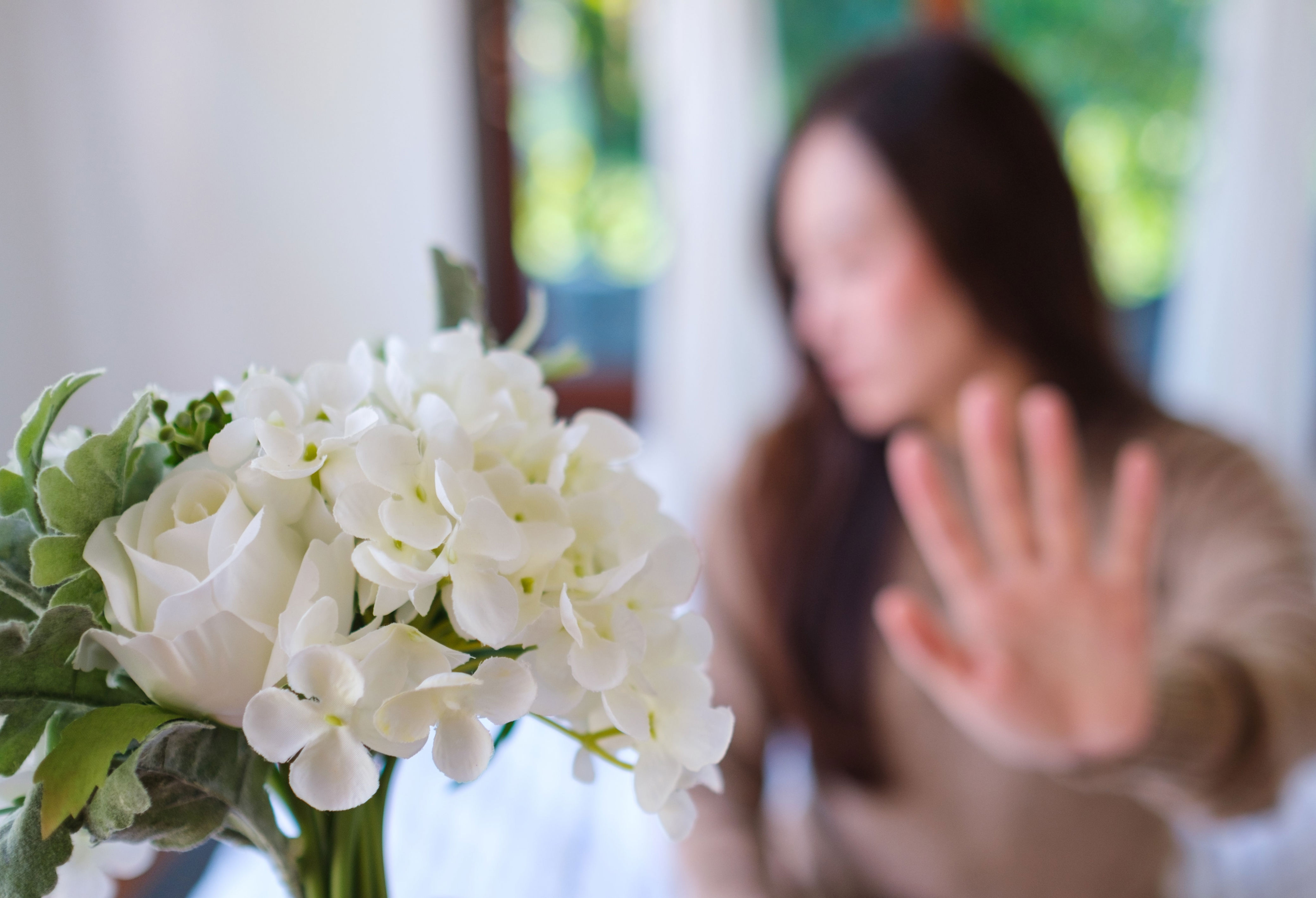 Person in focus holding flowers, out of focus person in background with hand raised in gesture of refusal