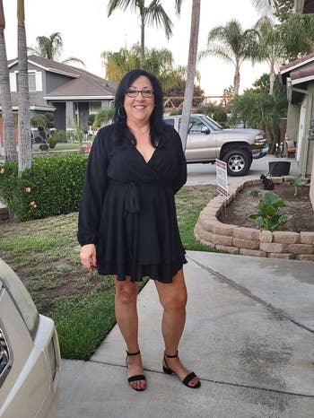 reviewer in black wrap dress and sandals smiling in a suburban driveway with palm trees in the background