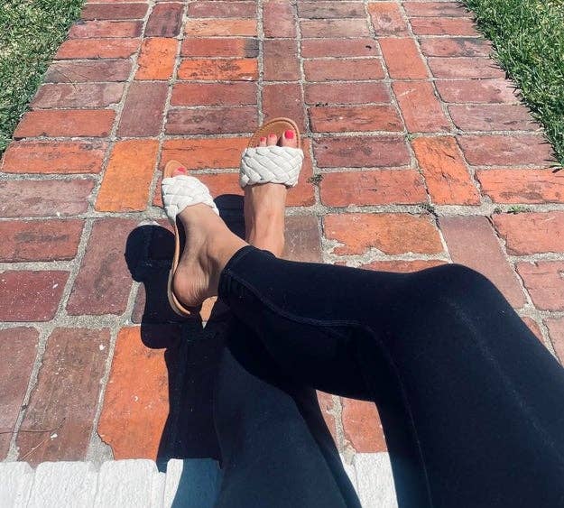 reviewer's legs in black leggings with woven sandals, crossed while seated on a brick path