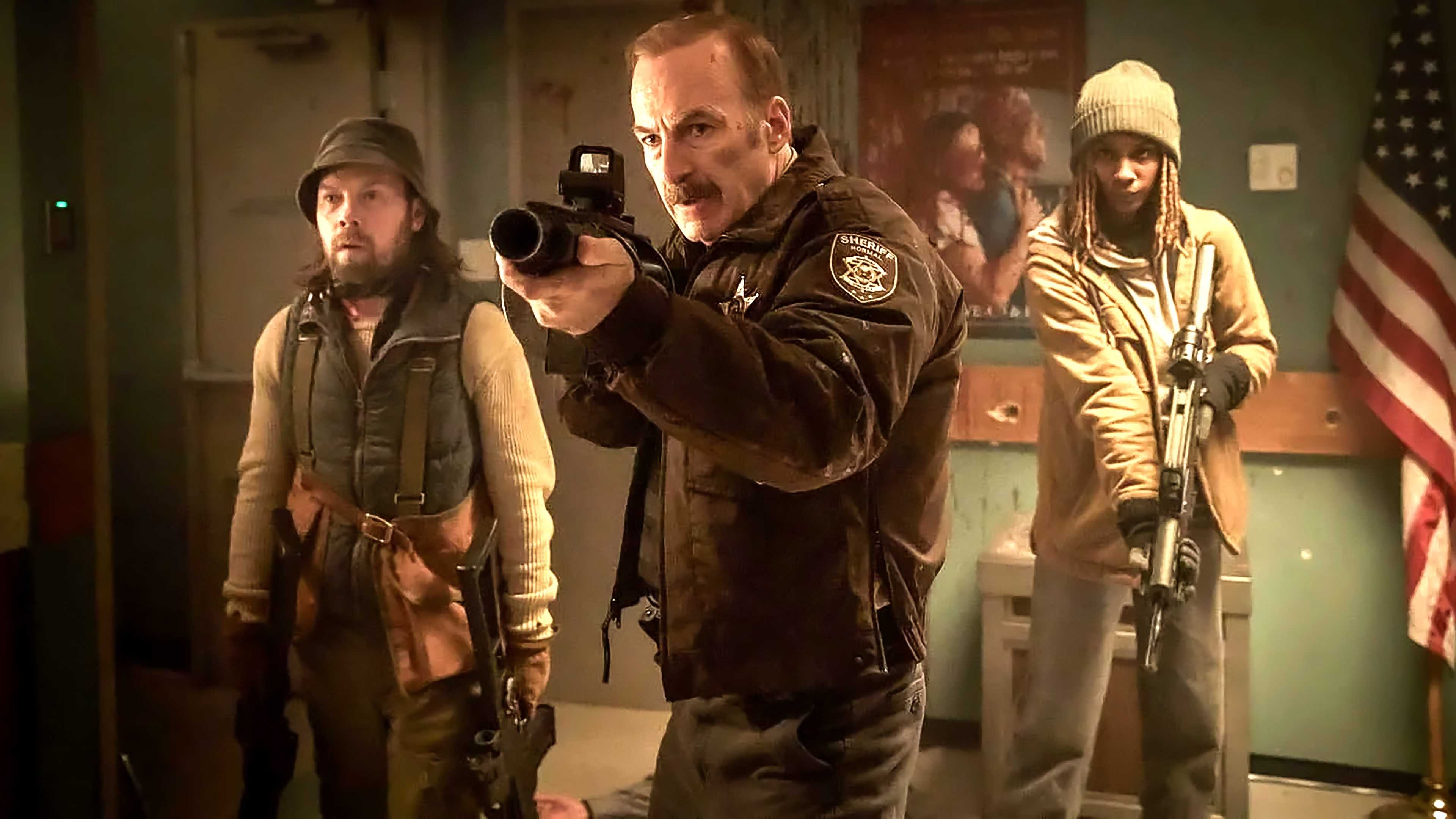 Bob Odenkirk's Ulysses looking intense and aiming a grenade launcher while standing in front of two people in Normal