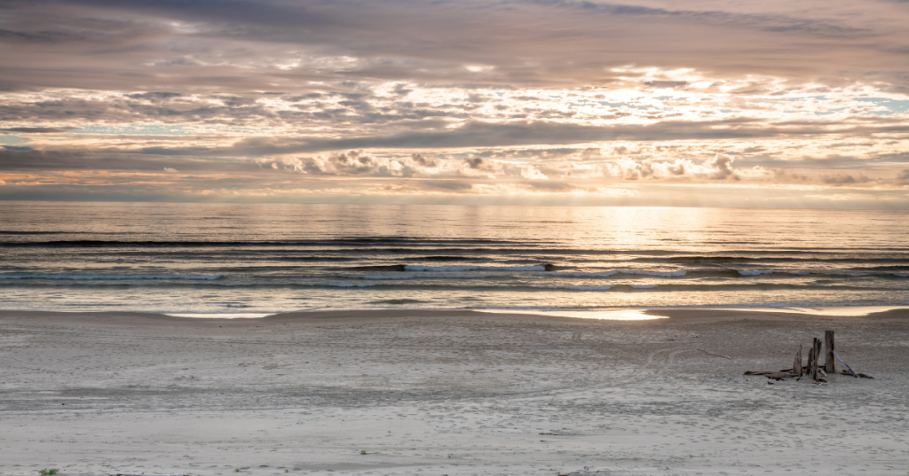 A serene beach scene at sunset near Waldport, Oregon, featuring gentle waves lapping at the shore under a colorful sky filled with clouds.