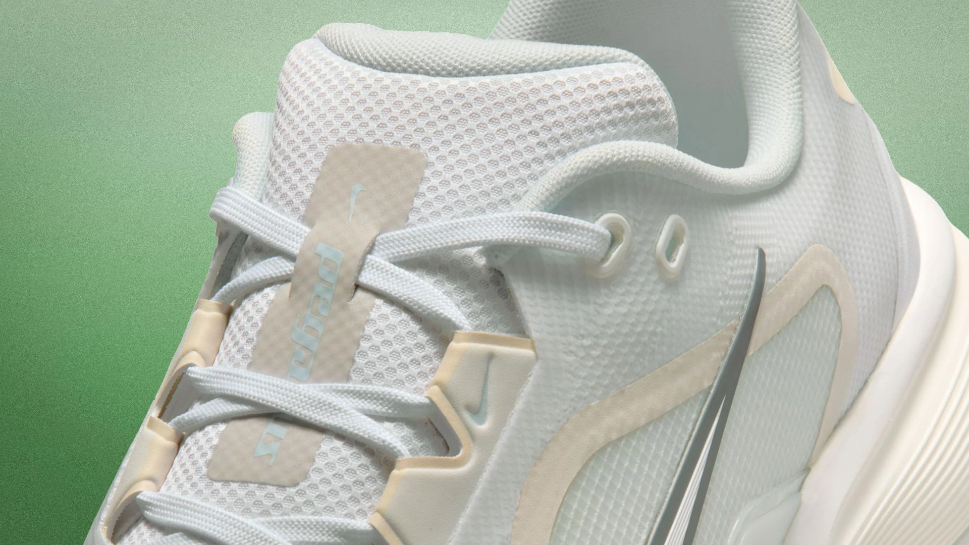 Close-up of a white Nike sneaker with mesh fabric, light beige accents, and white laces against a green background.