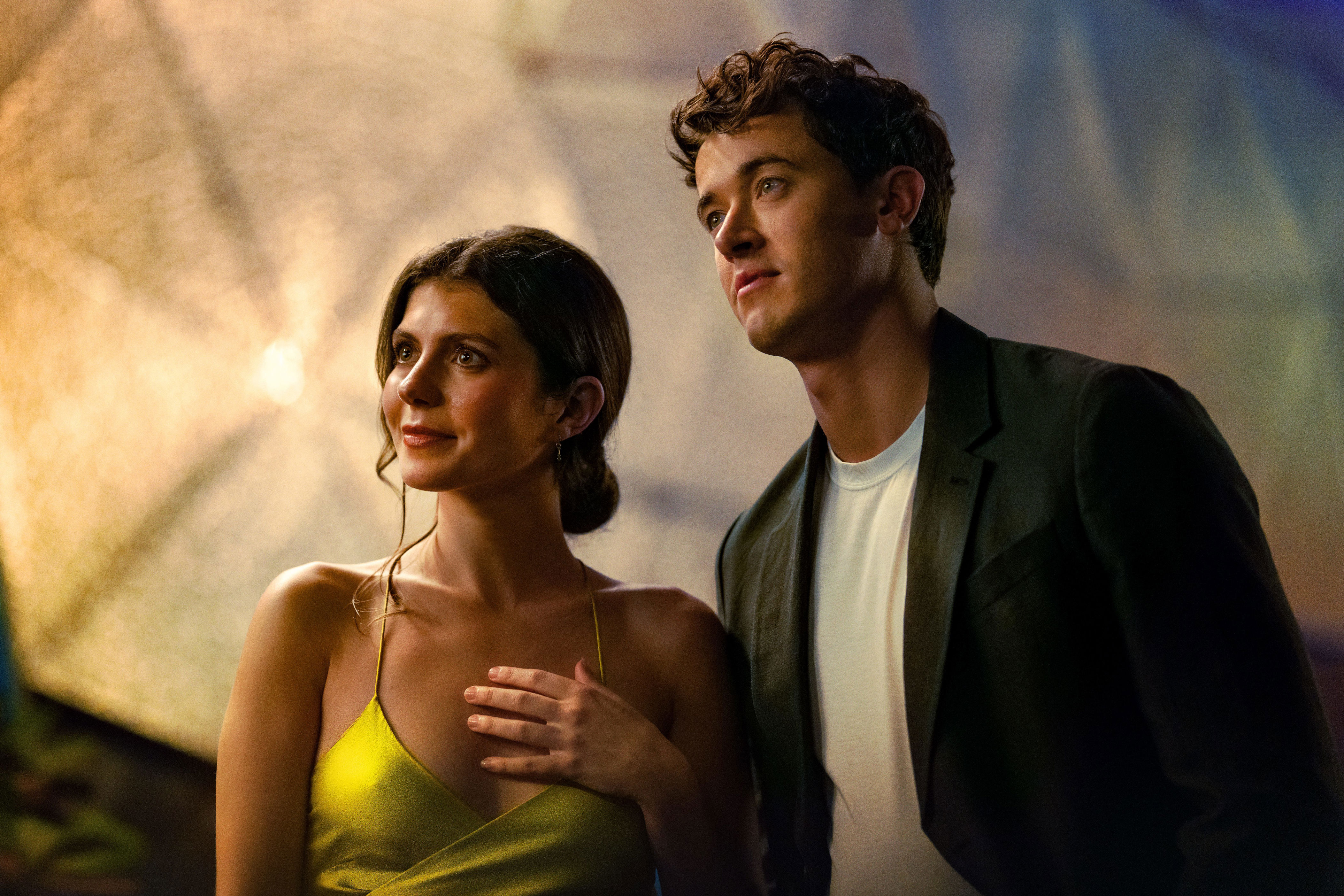 Emily Bader as Poppy wearing a bright yellow dress and Tom Blyth as Alex wearing a black blazer and white tshirt in People We Meet on Vacation