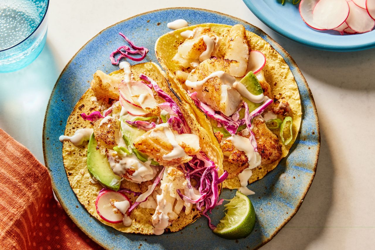 A plate with two fish tacos topped with shredded cabbage sauce and slices of lime on the side