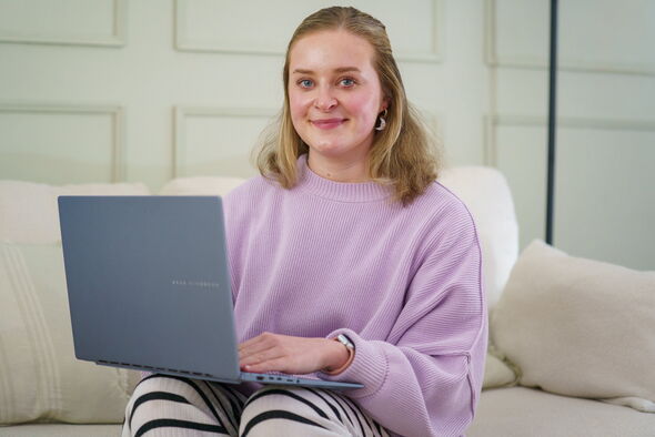 A woman sits on a sofa with her laptop