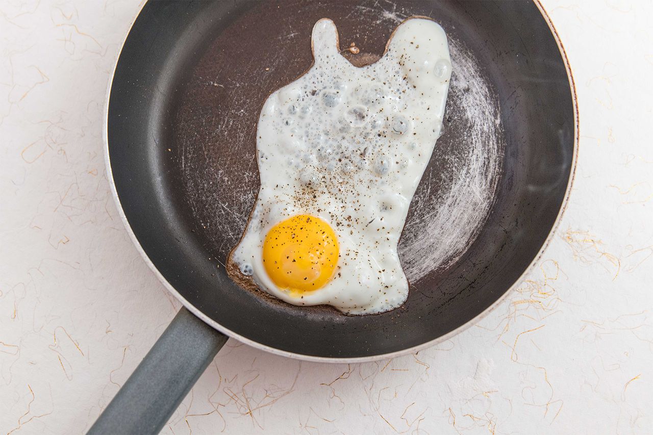 A fried egg in a frying pan with signs of wear and staining on the surface