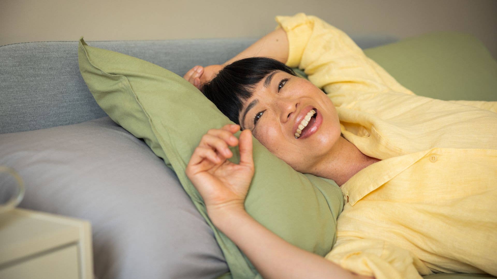 Woman laying in bed with green pillows in yellow pajamas enjoying the morning at home