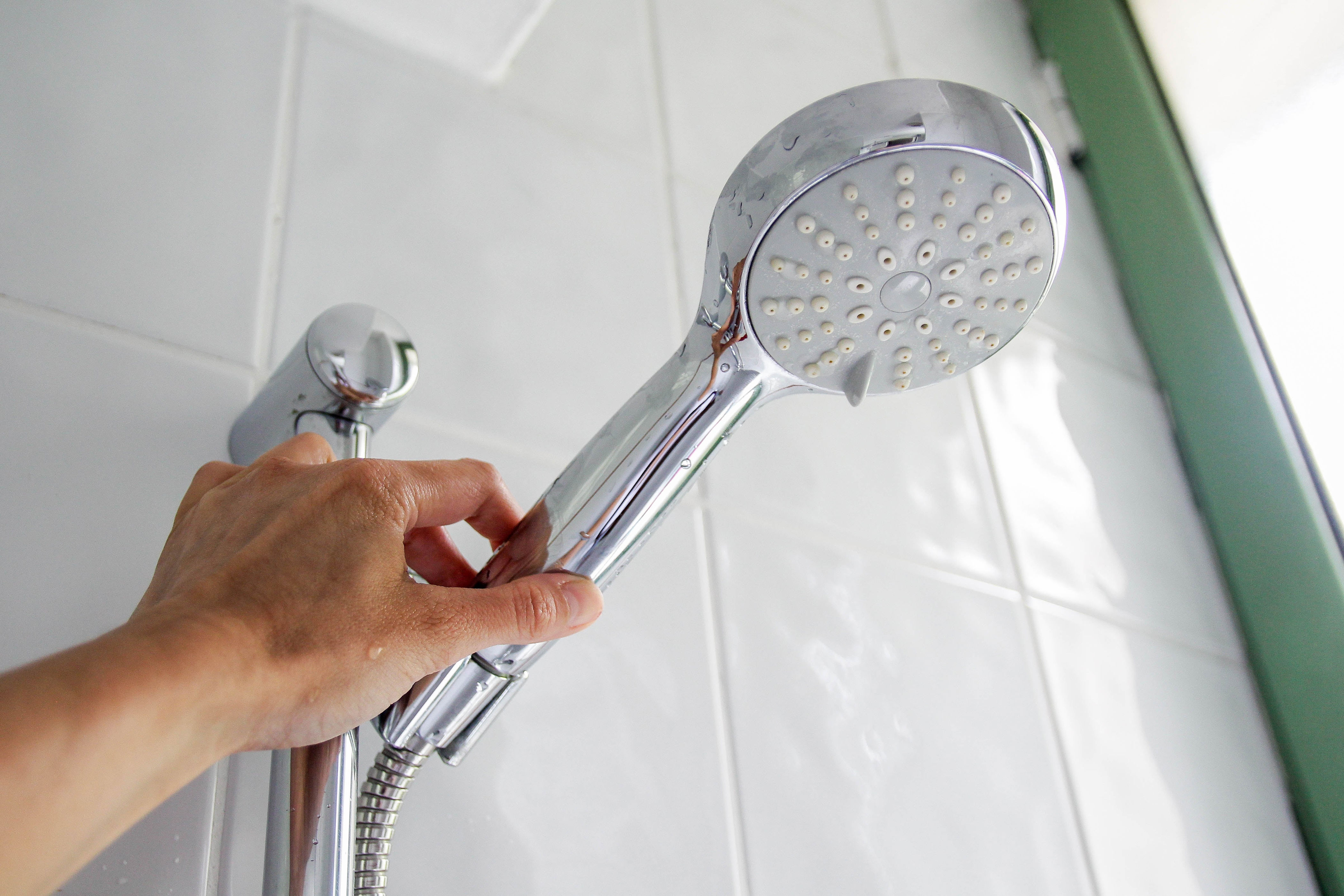 Hand adjusting a detachable showerhead on a tiled bathroom wall
