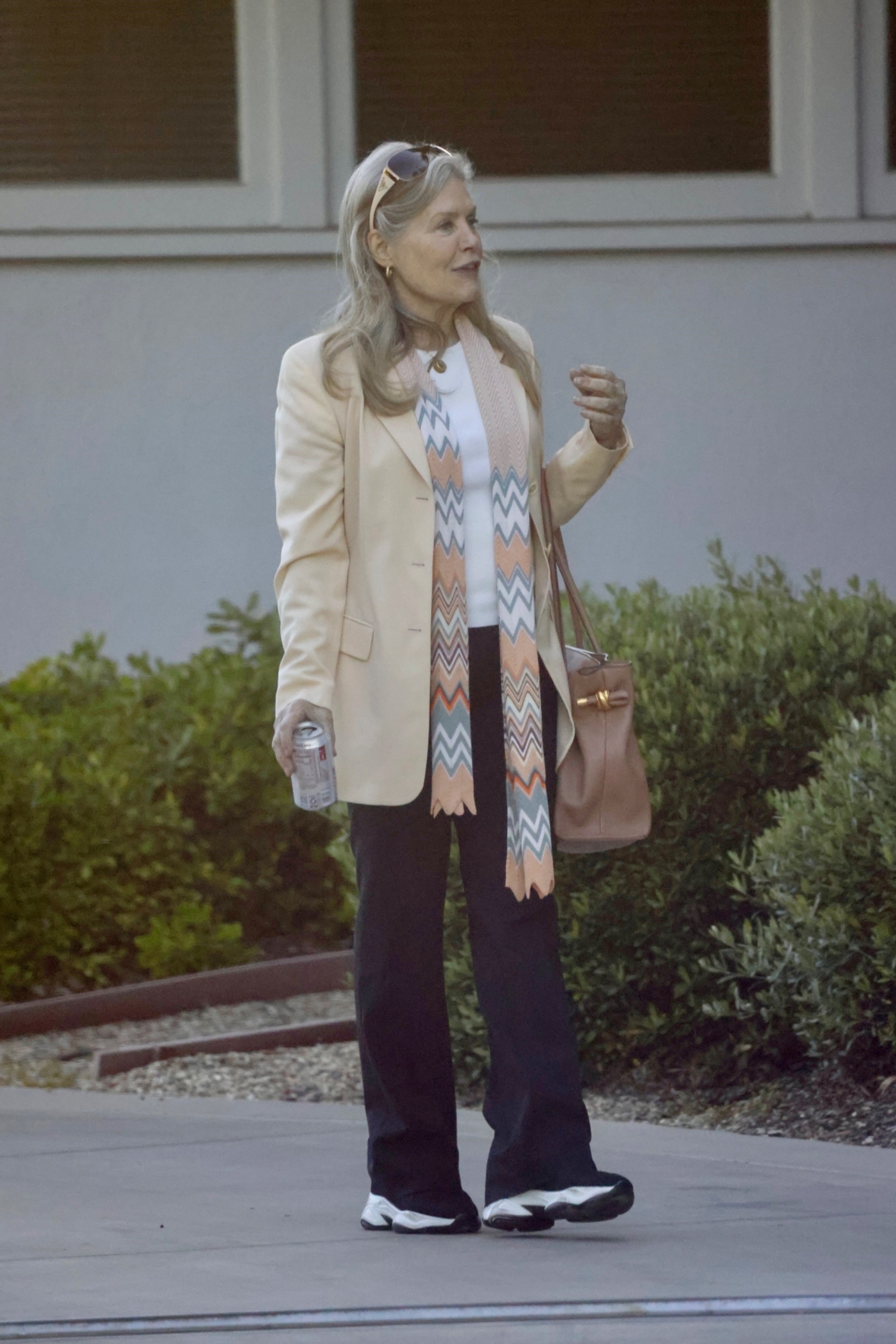 Beverly D’Angelo in a cream blazer and a chevron scarf, holding a soda can.