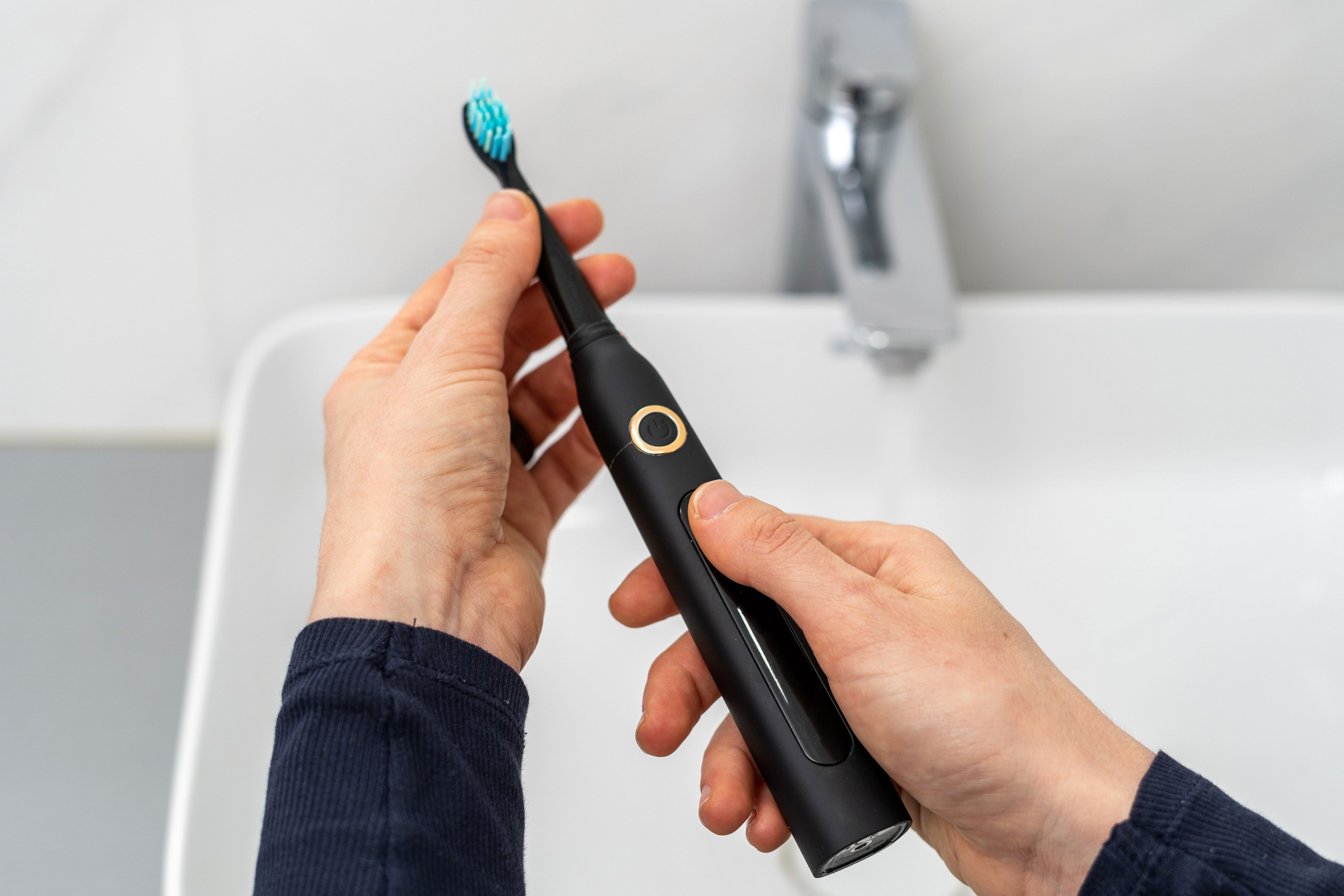 Person holding a black electric toothbrush over a bathroom sink