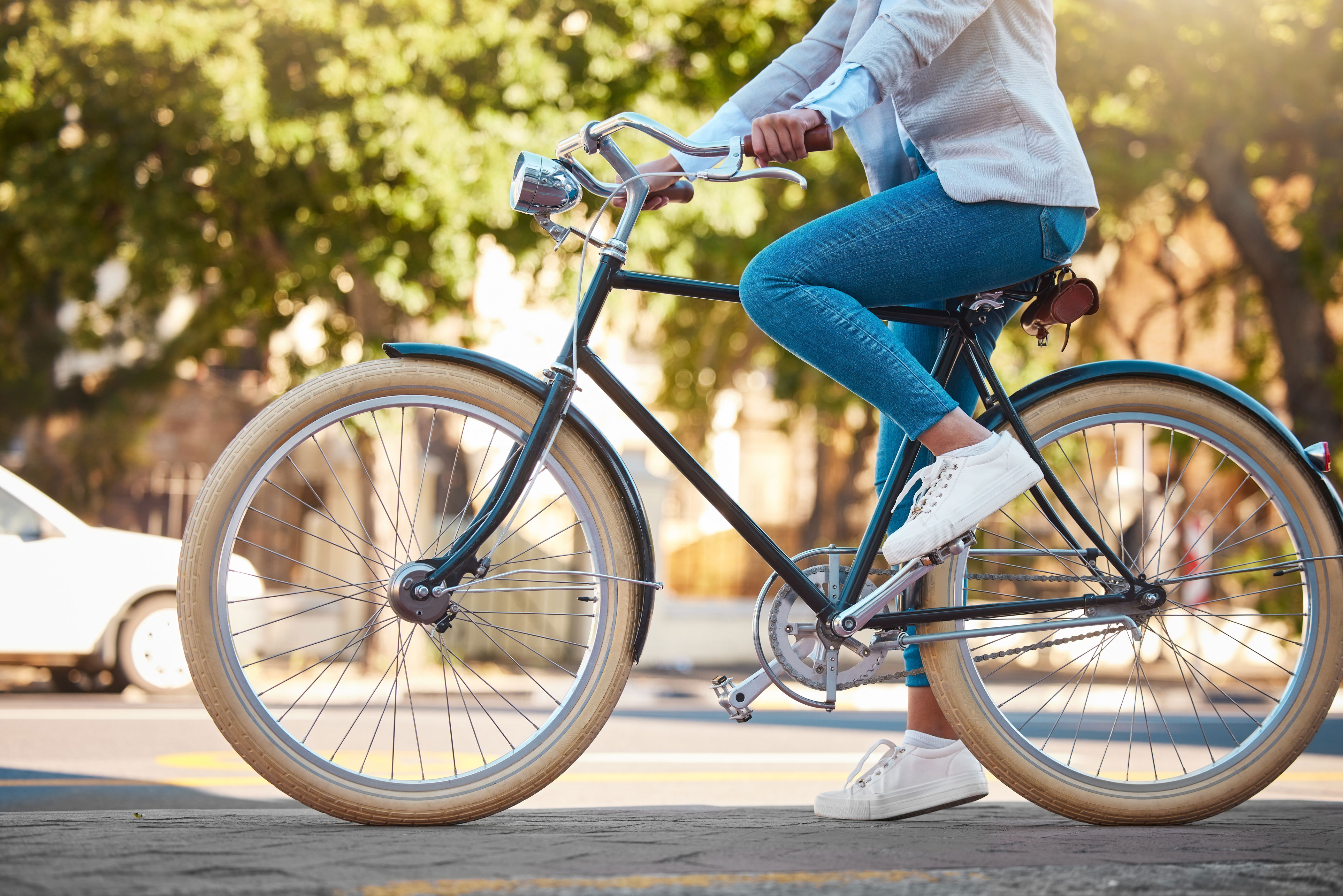Person in casual attire riding a bicycle on a tree-lined street, showcasing eco-friendly commuting