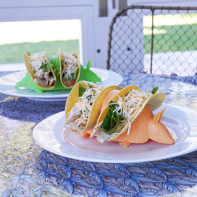 Tacos with shredded chicken and greens are displayed on armadillo-shaped holders, set on plates for a fun dining experience