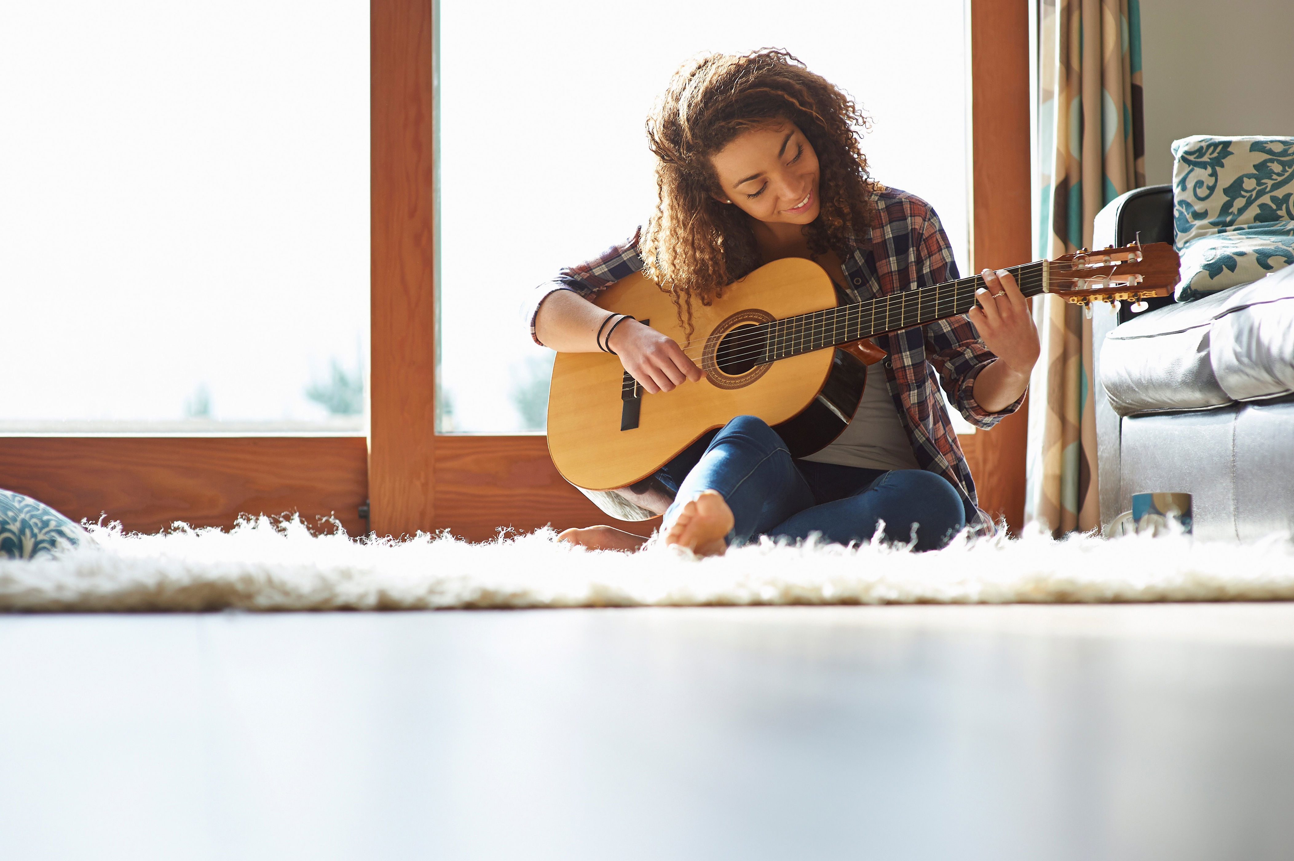 Person sitting on a rug in a living room, playing an acoustic guitar, appearing relaxed and focused