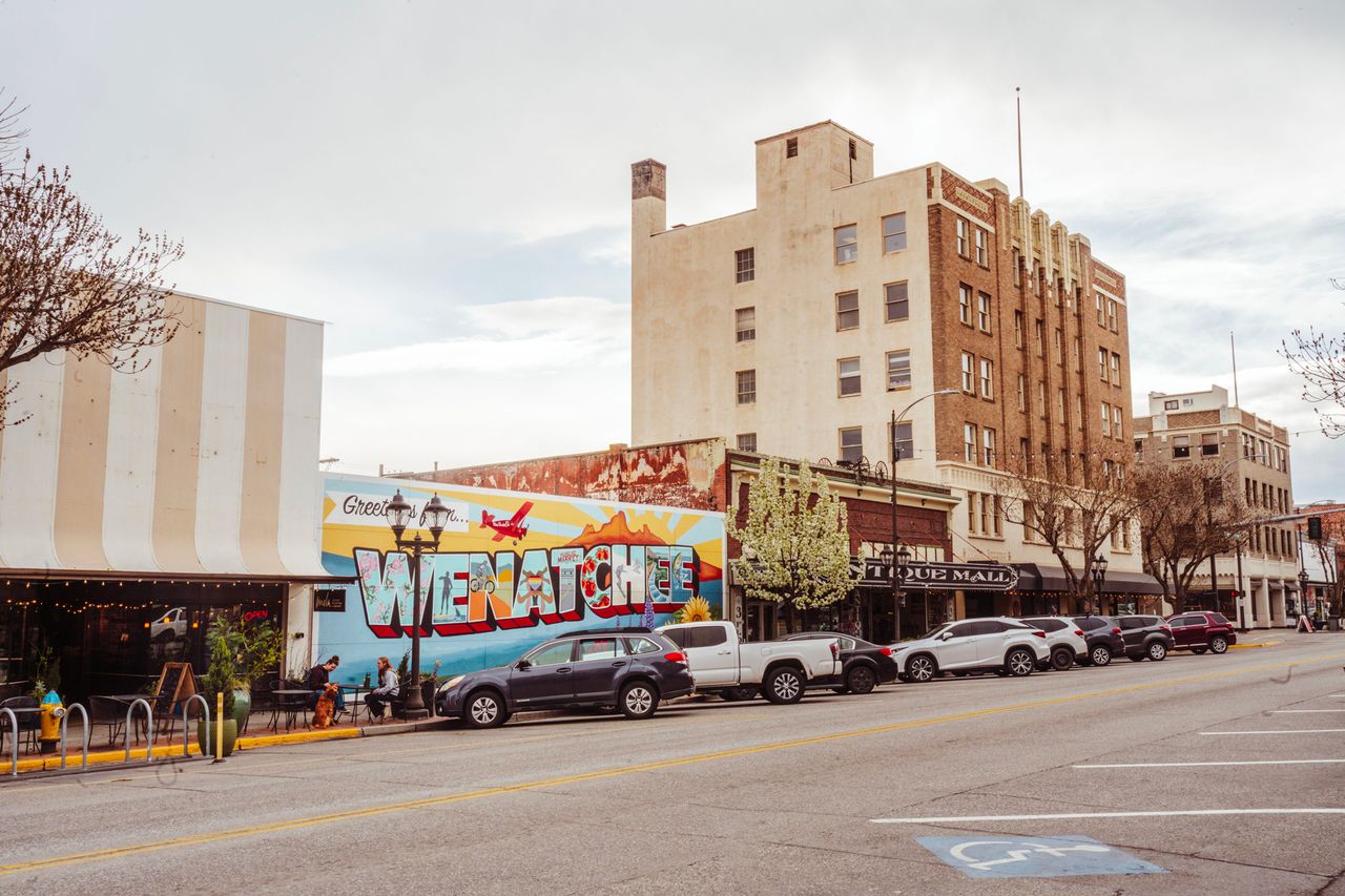 Street view with a mural saying Welcome to Wenatchee parked cars and midrise buildings in the background urban scene