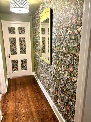Hallway with patterned floral wallpaper, wooden floor, a white door with glass panels, and a wall mirror
