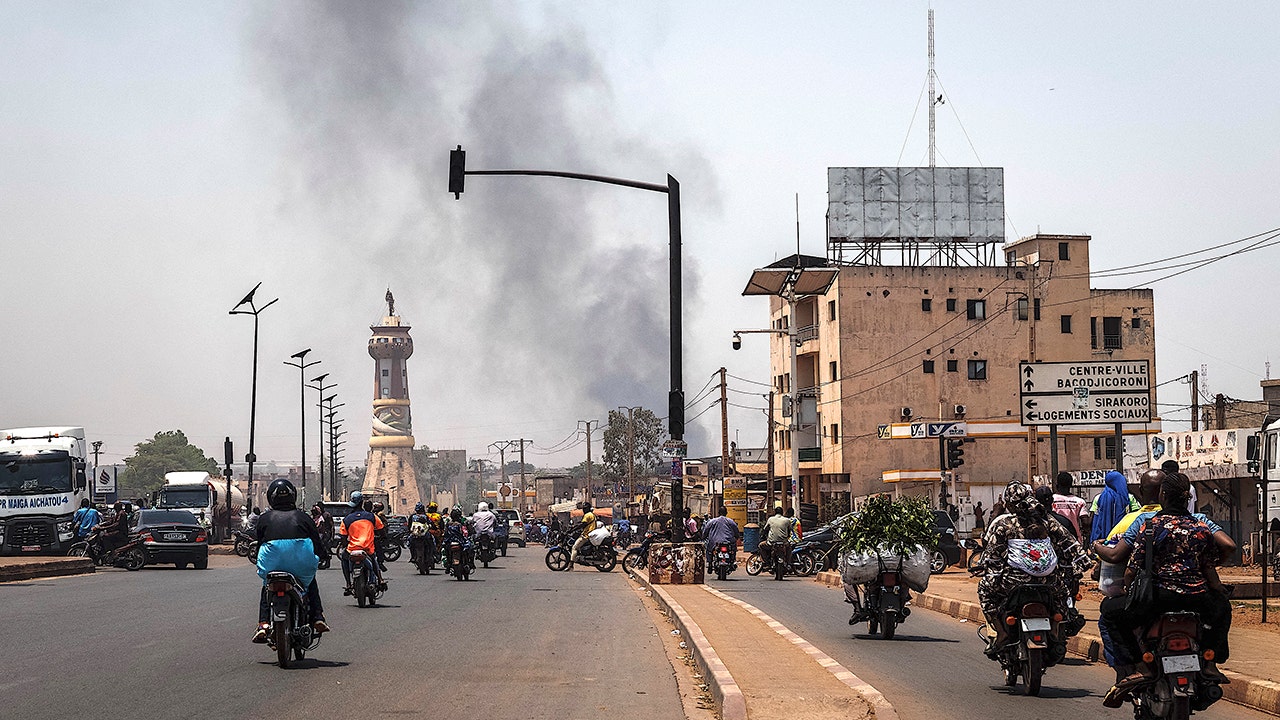 A column of black smoke rises above buildings as traffic passes the Africa Tower monument in Bamako on April 26, 2026. April 25, 2026's shock attacks, synchronized by Tuareg rebels of the Azawad Liberation Front (FLA) coalition and the jihadist Group for the Support of Islam and Muslims (JNIM), targeted several areas in the vast arid country. Fighting resumed on April 26 in several areas, including Kita near Bamako, Kidal, Gao and Severe.Tuareg rebels meanwhile announced an agreement allowing Russian forces backing Mali's army to withdraw from the northern city of Kidal, which they claimed was "totally" under their control.