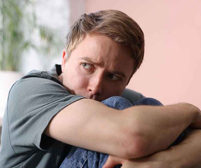 A young man in a gray t-shirt and jeans, looking anxious, contemplating the sacrifice of life for disabled siblings.