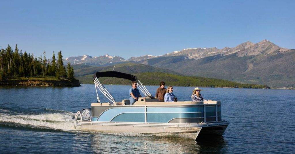 Four people cruising along in a pontoon boat, enjoying a day on Dillon Reservoir, surrounded by mountain peaks and evergreen trees in Dillon, Colorado.