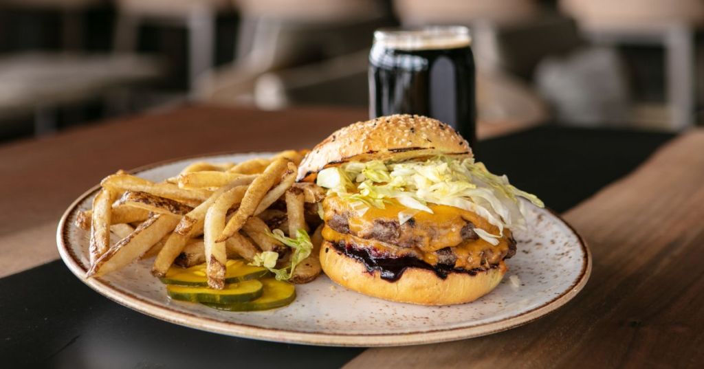 A juicy double-patty burger with melted cheese, shredded lettuce, and sauce soaking the bun, served with pickles and a side of fries at VUE Rooftop in Dillon, Colorado